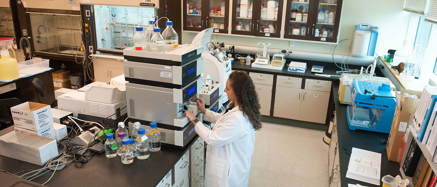 A female student in lab coat standing in a pharmacy lab.a pharmacy lab.